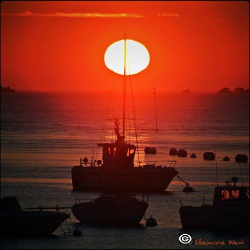 Coucher de soleil traversé par le mât d'un petit bateau de pêche à contre jour. Ciel rouge. Aber Ildut- Finistère- Bretagne- France