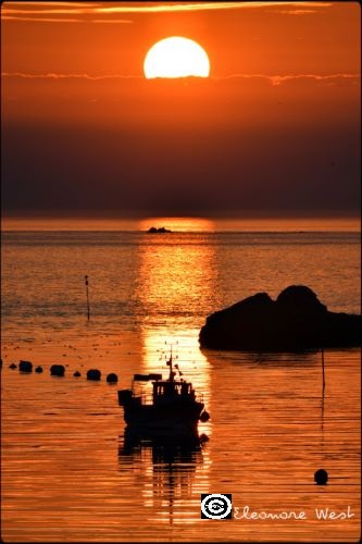 Coucher de soleil qui donne une lumière orange à l'image. Petit bateau de pêche, un rocher, l'entrée de l'Aber Ildut composent cette photo. Finistère- Bretagne-France
