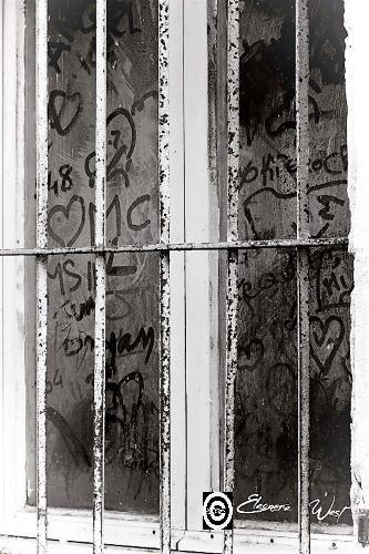 Derrière les barreaux, une fenêtre en bois blanc usé. La vitre sale a permis de nombreux messages tracés au doigt. Des coeurs, des lettres. Détail d'une ruelle de Sigean- Aude- Occitanie- France