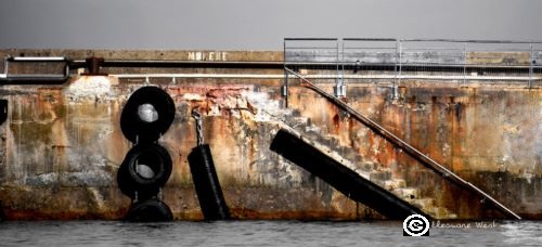 Quai de l'île Molène en gris et ocre marron. Le petit escalier de débarquement côtoie 2 pneus noirs. Format panoramique. Finistère- Bretagne- France