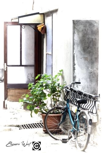 Ruelle de Sigean- Aude- Occitanie- France Effet dessin. Une porte ouverte. Une plante en pot. Une bicyclette bleue. Des murs gris et blancs